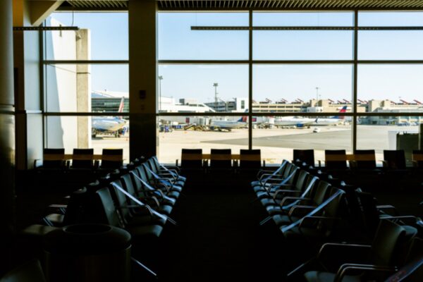 Empty rows of seats in an airport departure lounge, with aircraft parked outside the large windows